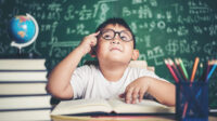 Thoughtful little boy with book in the classroom
